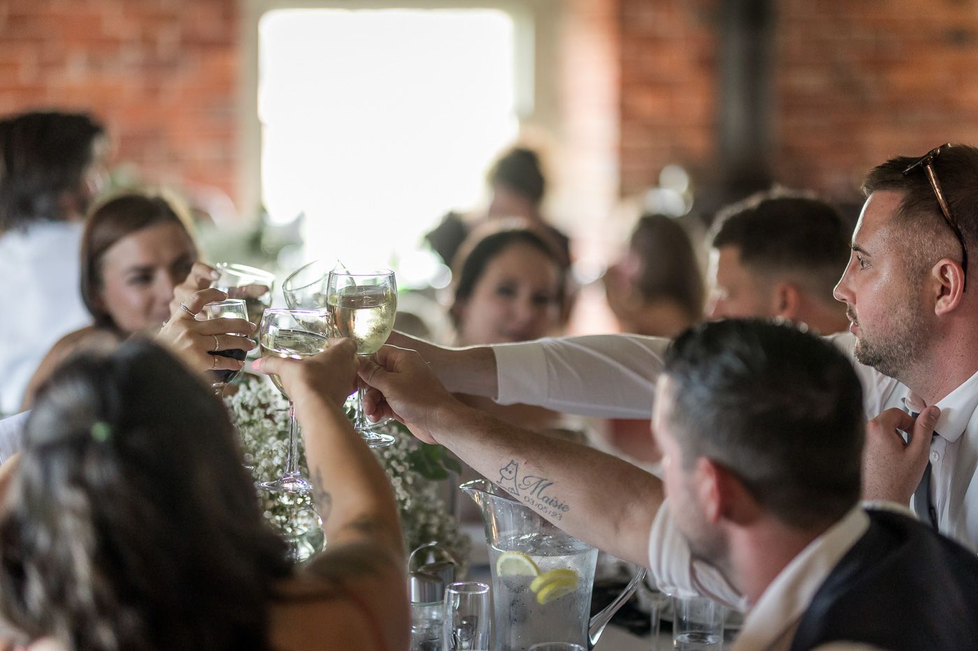Wedding reception guests seated at tables in a rustic brick-walled venue.