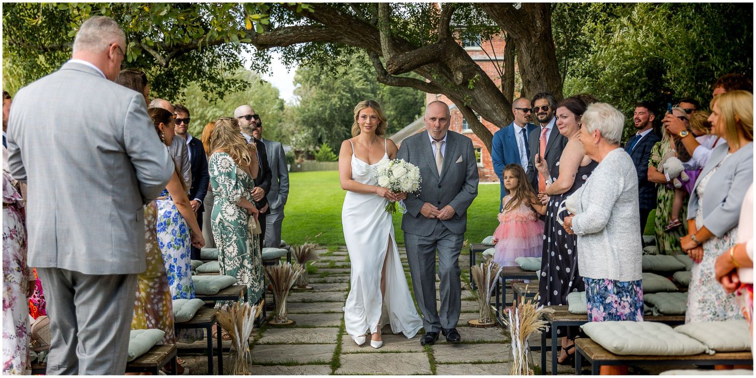 Outdoor wedding ceremony with guests seated on chairs along a stone path.