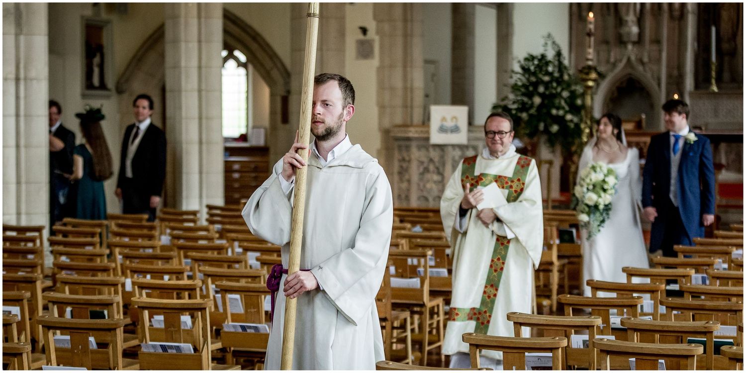 Church wedding ceremony with guests seated in wooden pews and sunlight streaming through windows.