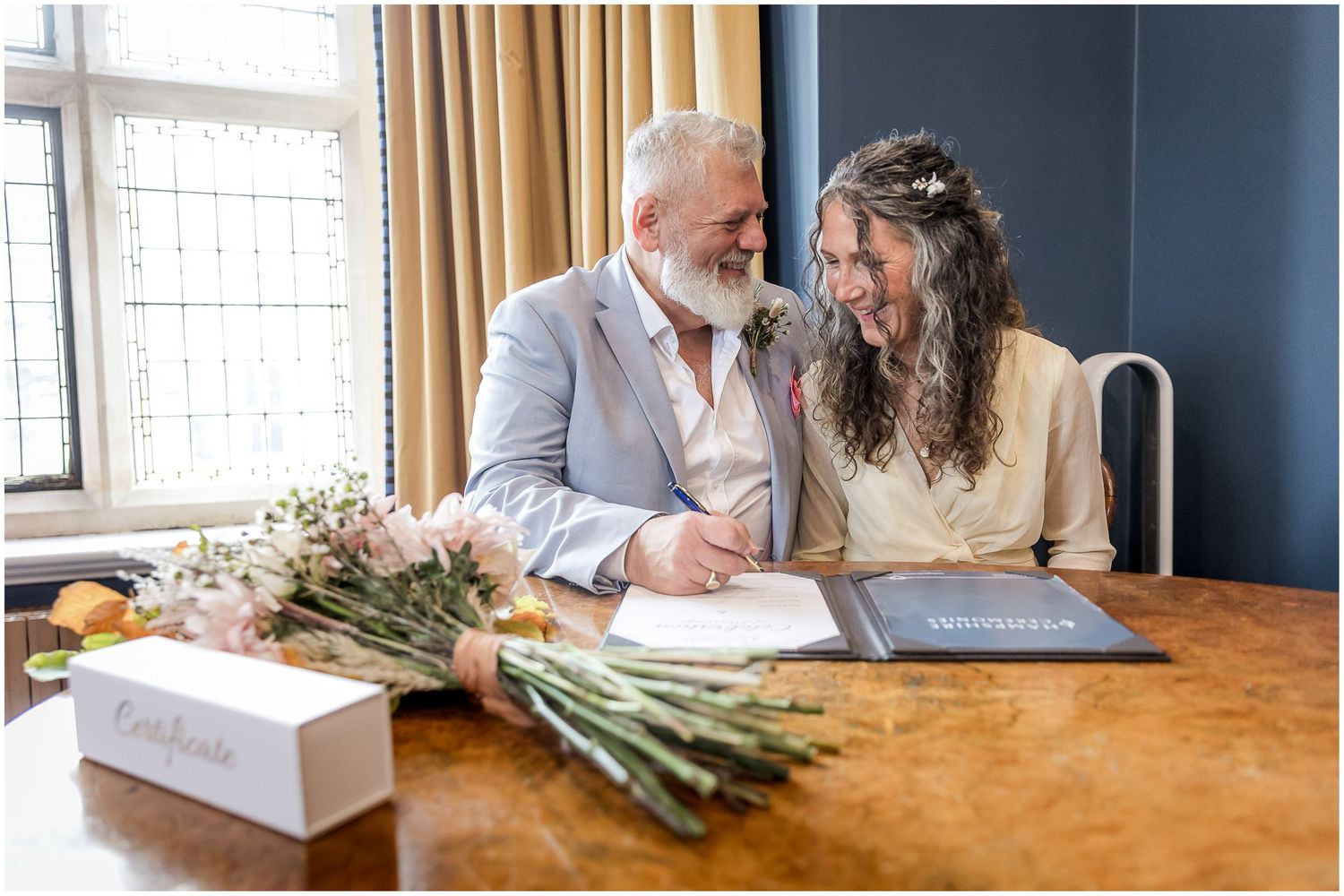 The bride and groom sit together to sign the certificate of marriage in Winchester registry office's Castle Room.
