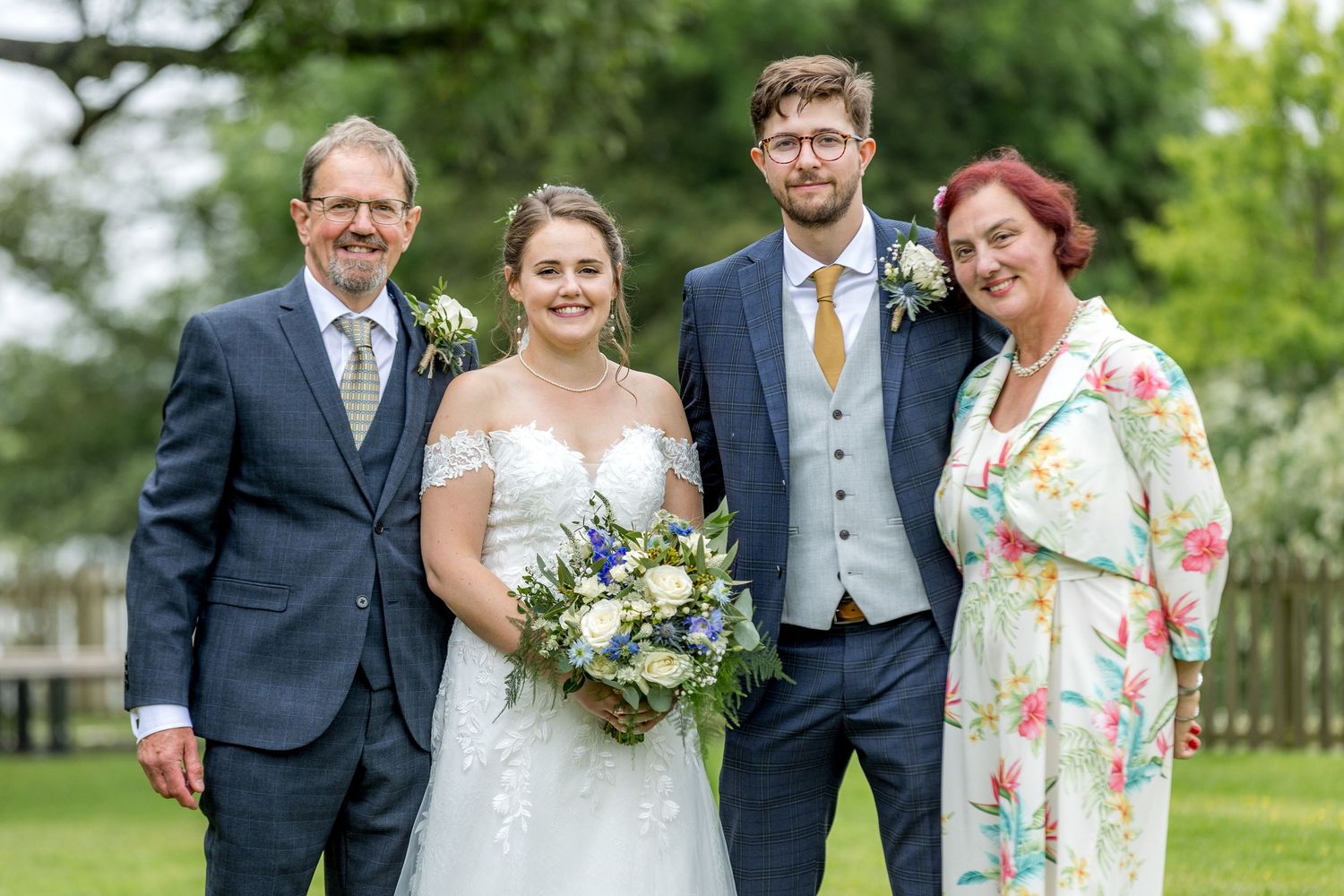 Wedding party gathers for formal portraits in a lush garden setting with floral bouquets.