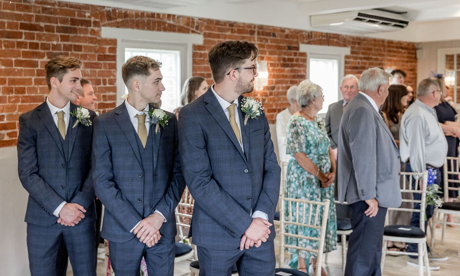 Wedding party and guests gathered in a modern venue with brick walls and natural lighting.