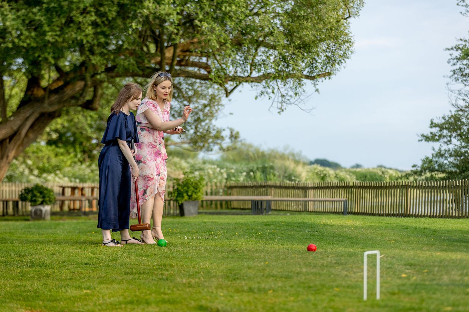 Garden lawn set up for croquet with hoops and guests in the background.