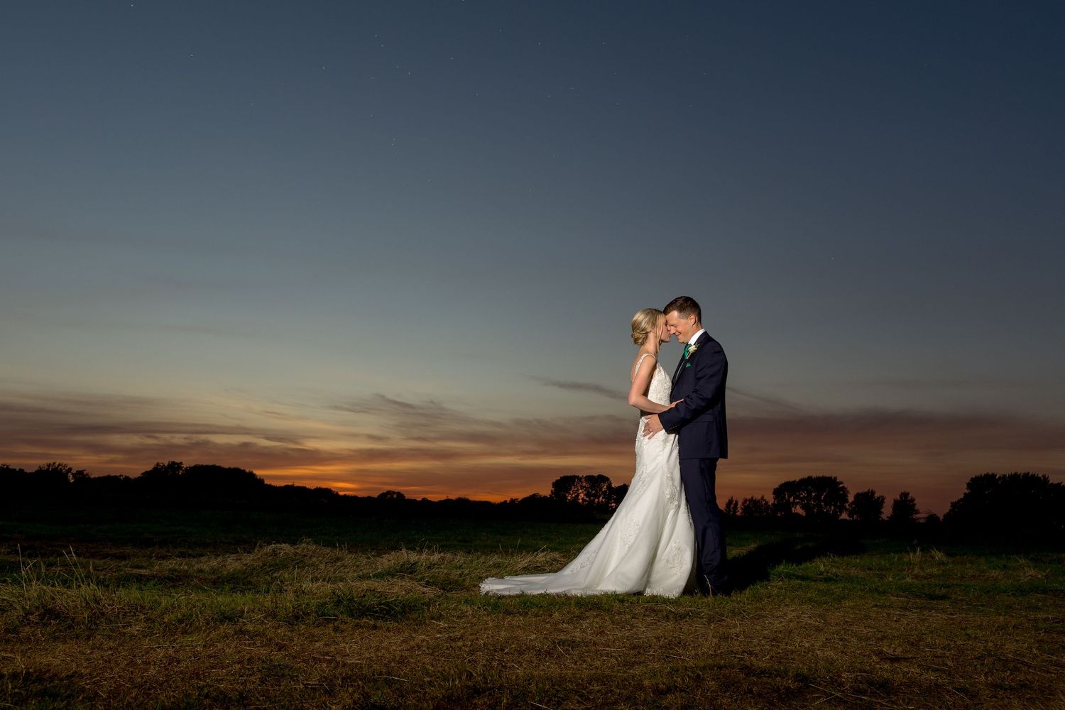 Romantic sunset silhouette of a couple embracing in an outdoor wedding setting.