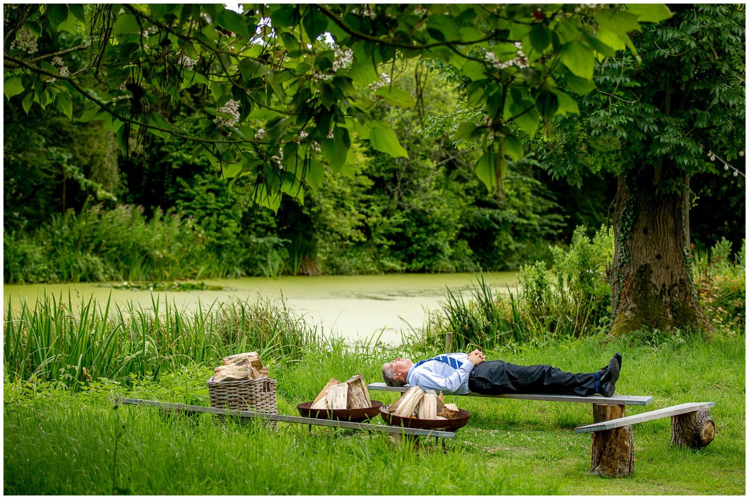 Two people relax on wooden benches in a peaceful garden setting surrounded by lush green foliage.