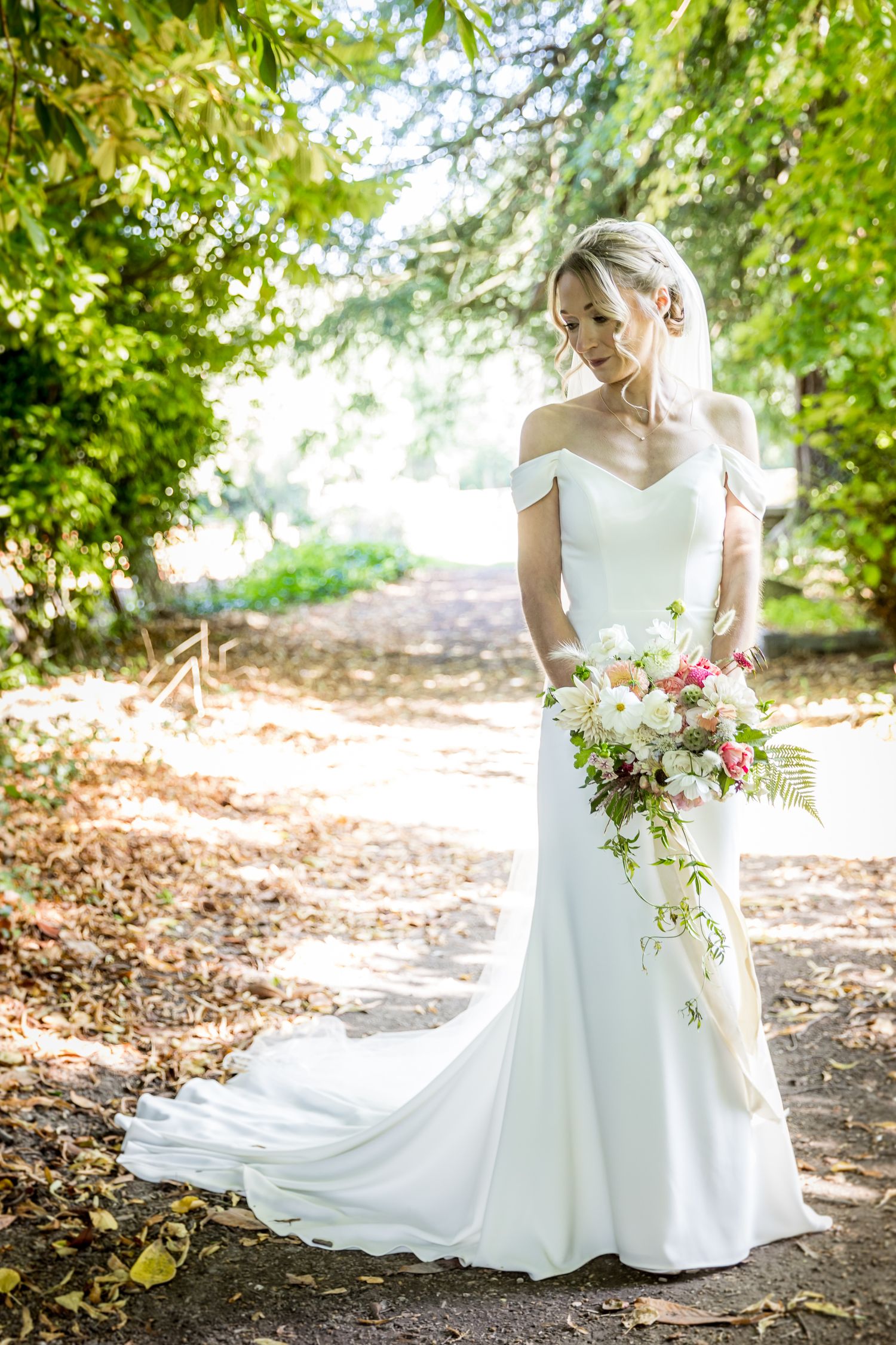 Elegant white wedding dress details with flowing train and floral bouquet in garden setting.