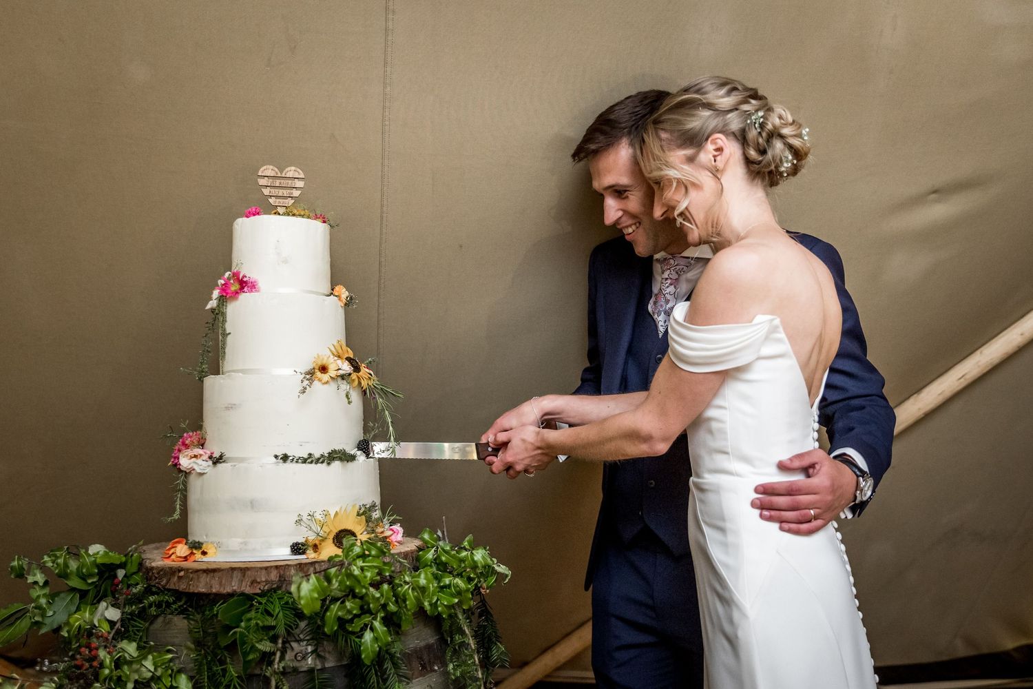 Wedding cake cutting moment captured inside a beautifully decorated tipi tent.