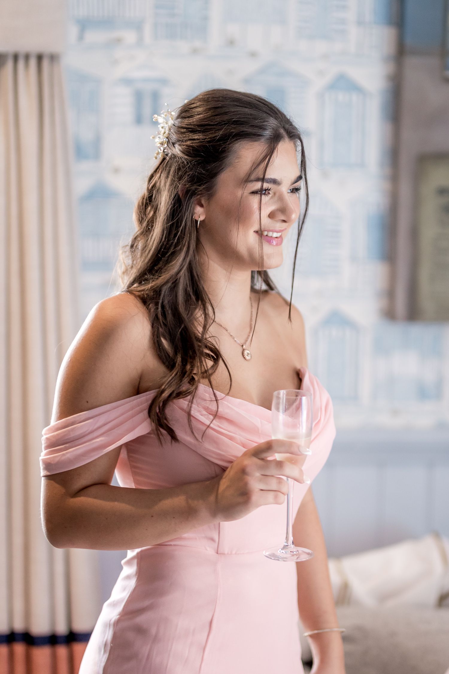Woman in a pink off-shoulder dress holding a champagne glass in an elegant room.