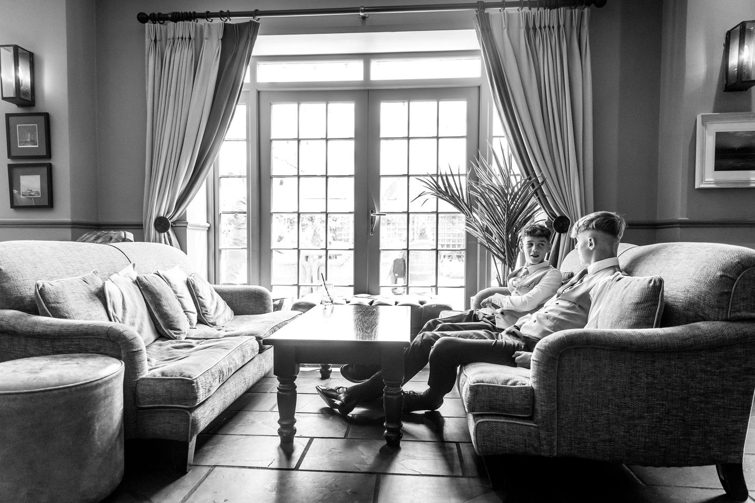 Cozy living room scene with people relaxing on comfortable sofas near large windows with elegant curtains.