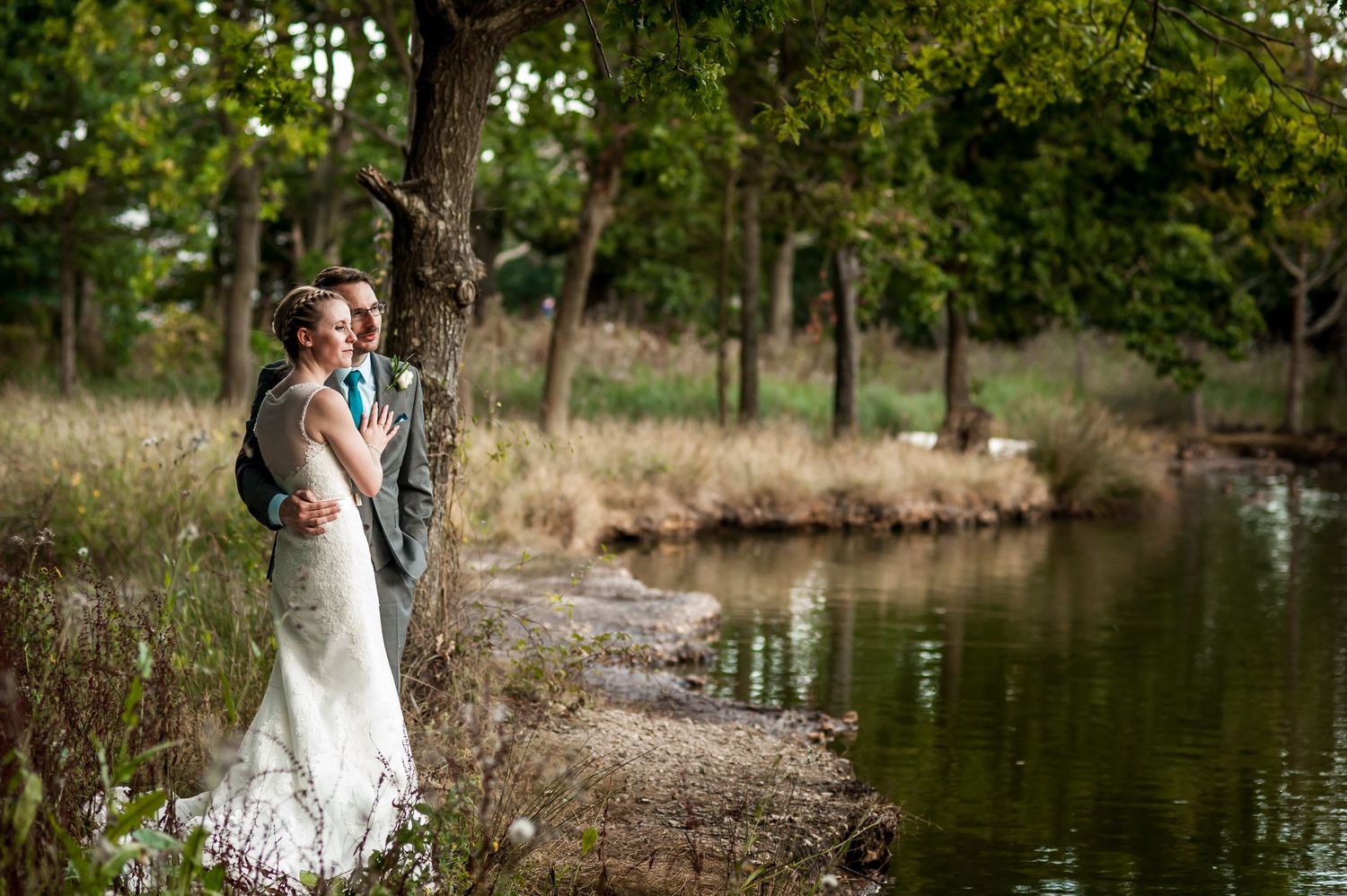 Couple walks along scenic pond with trees reflecting in calm water.