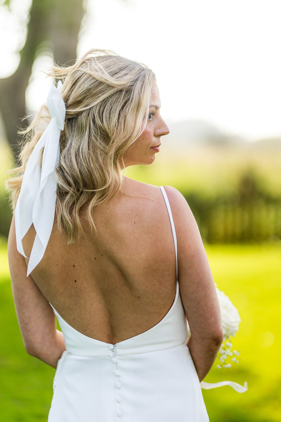 Back detail of a white wedding dress with tie straps against a sunlit natural background.
