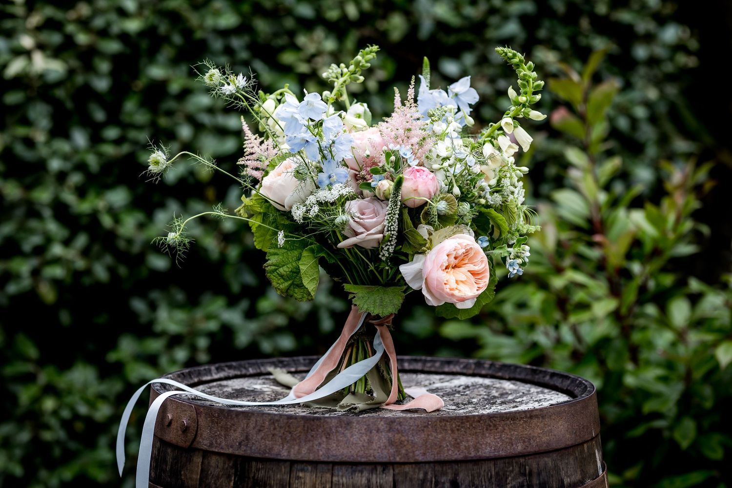 Delicate pink and white floral wedding bouquet rests on rustic wooden barrel.