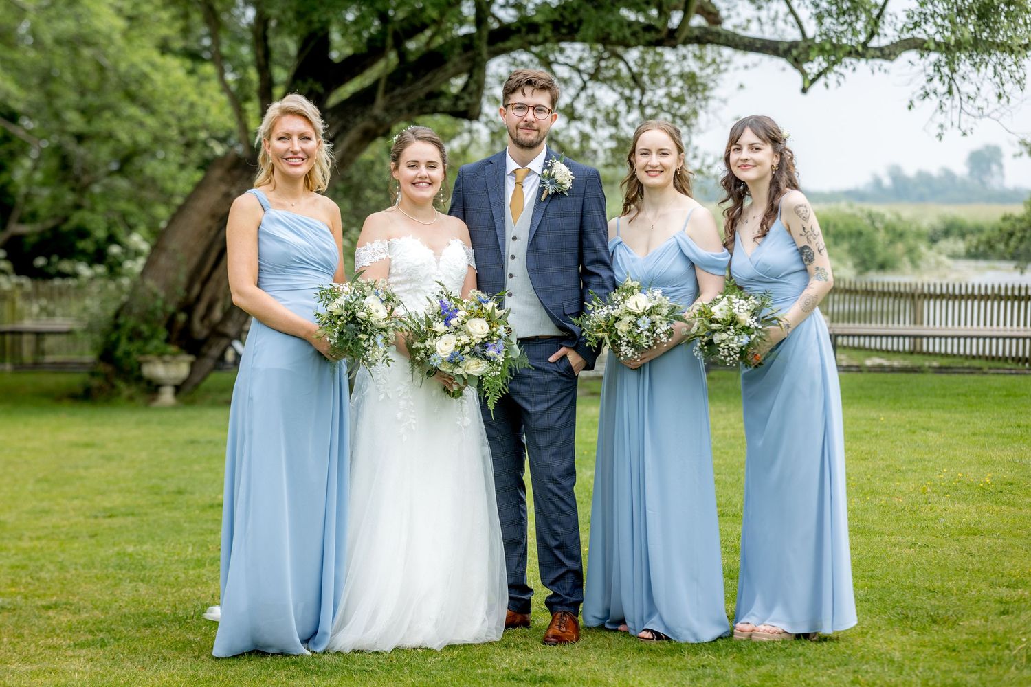 Bridesmaids in light blue dresses pose with bride on grassy lawn.