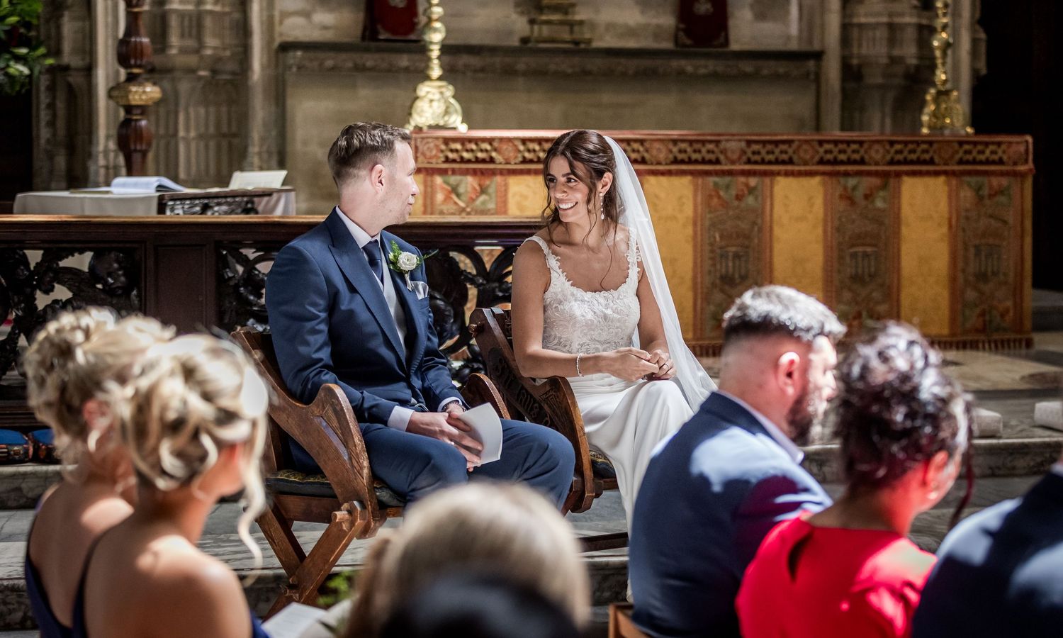 Wedding guests gather inside a grand cathedral with ornate Gothic architecture and vaulted ceilings.