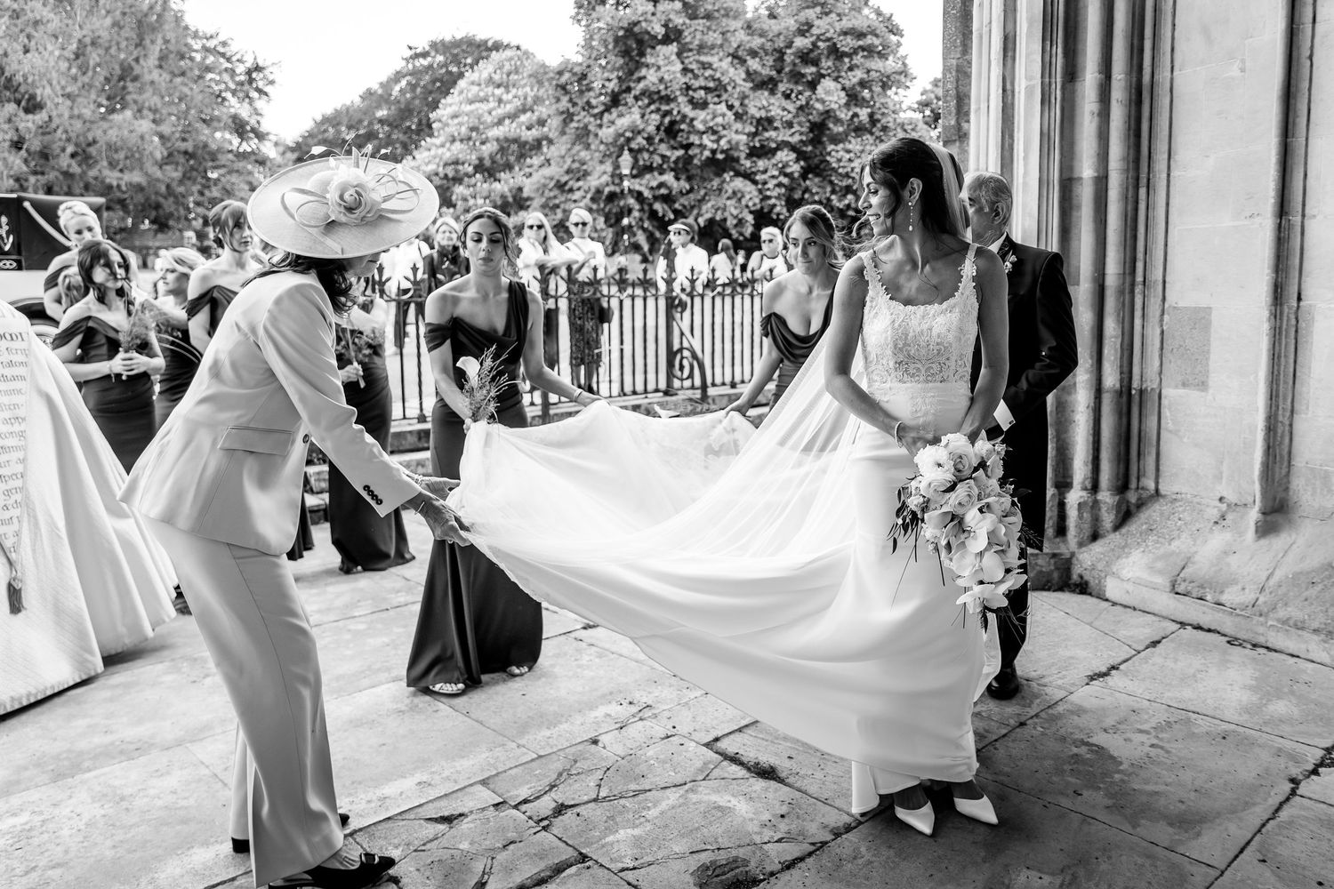 A flowing white wedding dress train billows in the wind during an outdoor photoshoot at a historic venue.