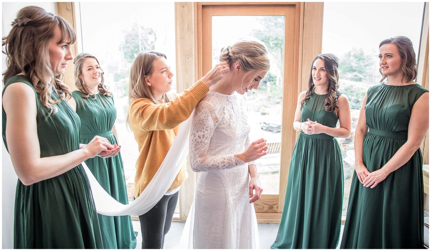 Wedding party members in emerald green dresses helping with bridal preparations.
