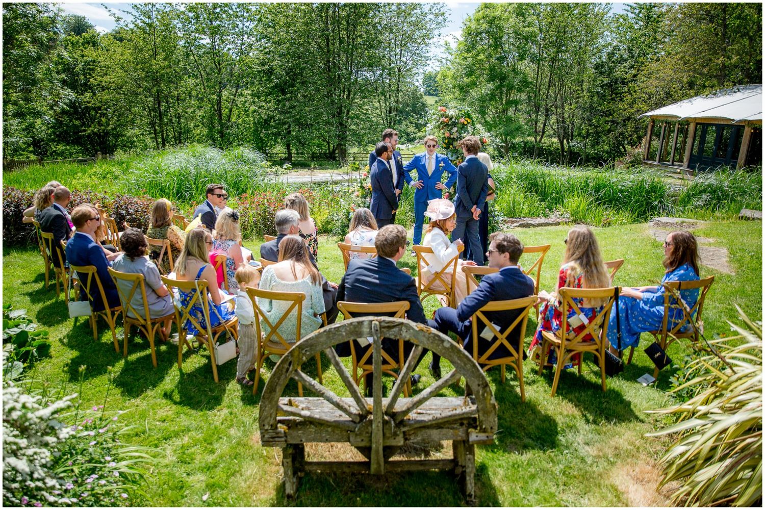 Guests seated in wooden chairs on a lush green lawn during an outdoor garden ceremony.