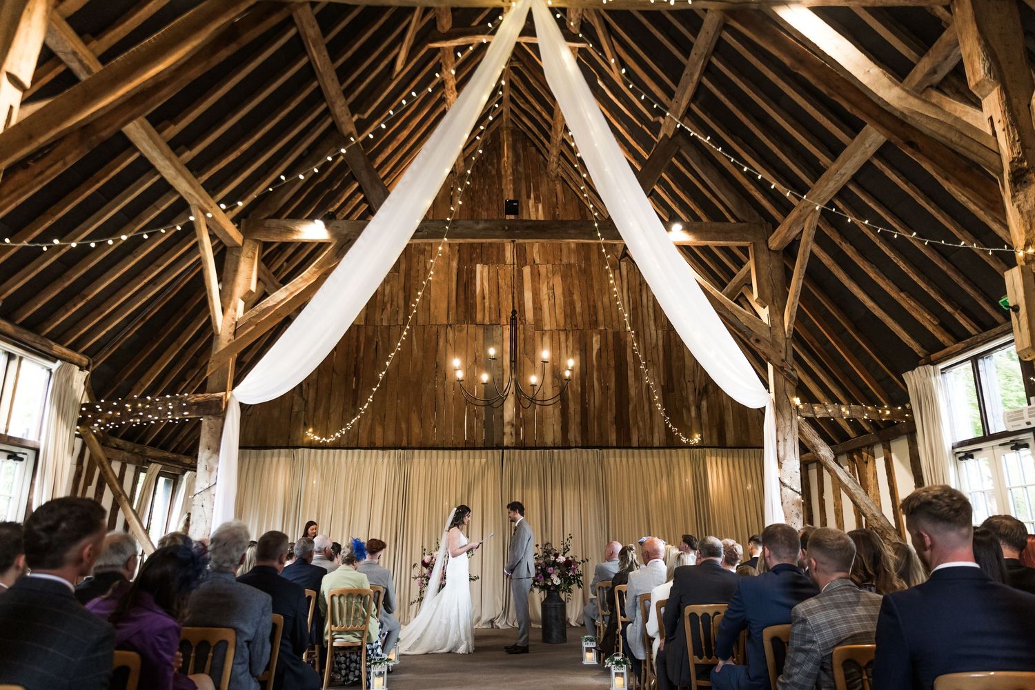 A wedding photograph of a marriage ceremony at Hampshire's Clock Barn, taken from the far end of the aisle at the rear of the barn