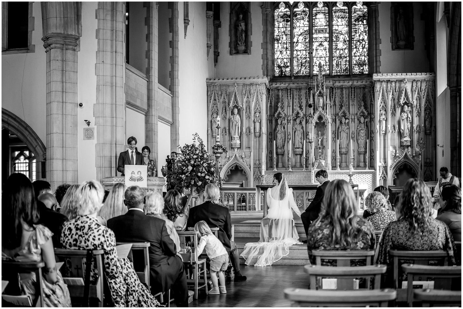 Black and white photograph of a wedding ceremony in a traditional church with stained glass windows.