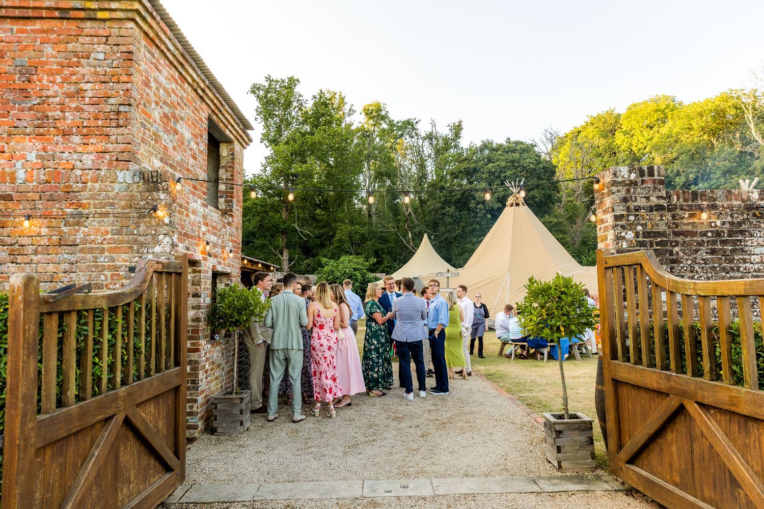 Brick wall entrance with wooden gates leading to tipi tents set up for an outdoor event.