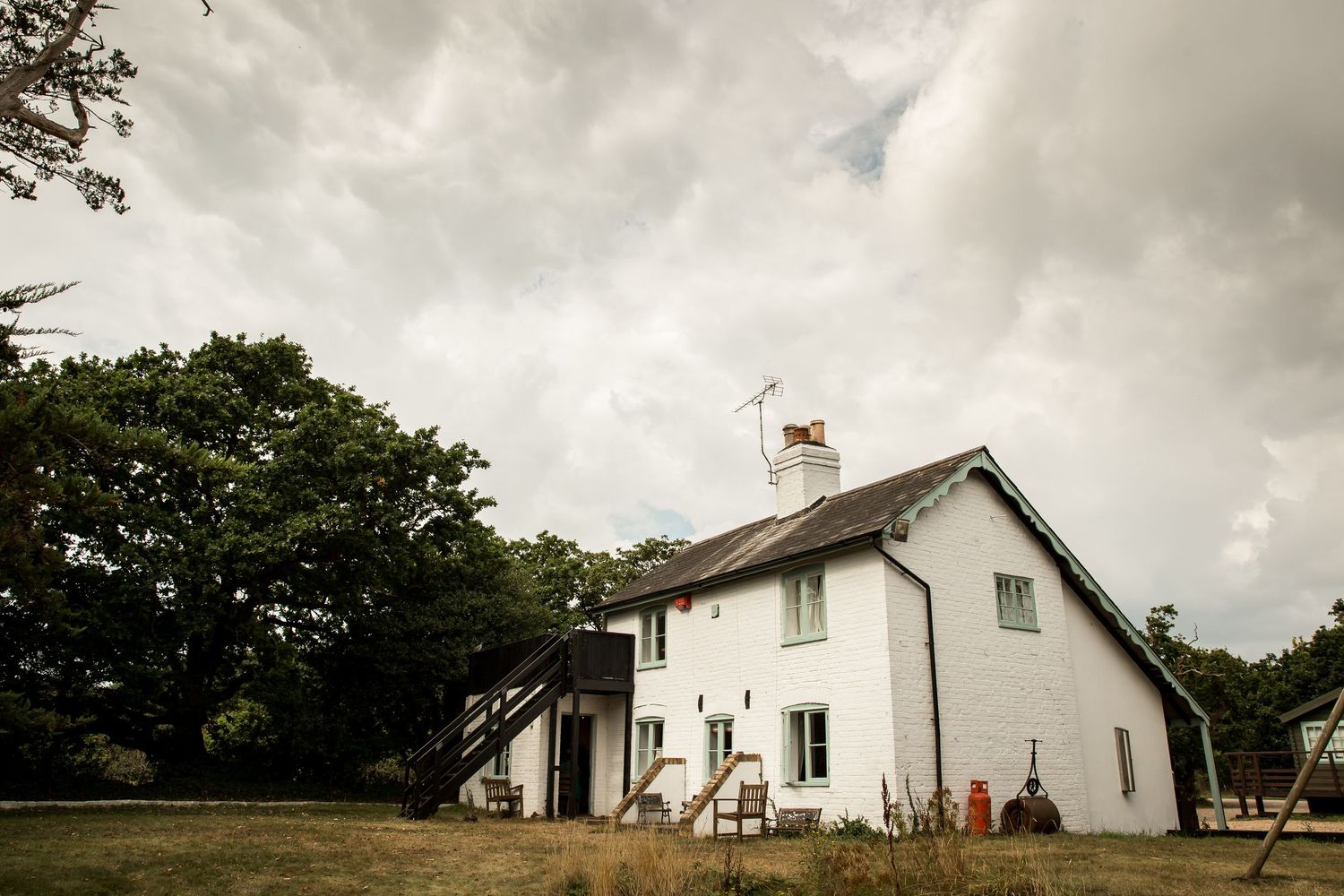 Row of white farmhouse buildings under cloudy skies in rural setting.