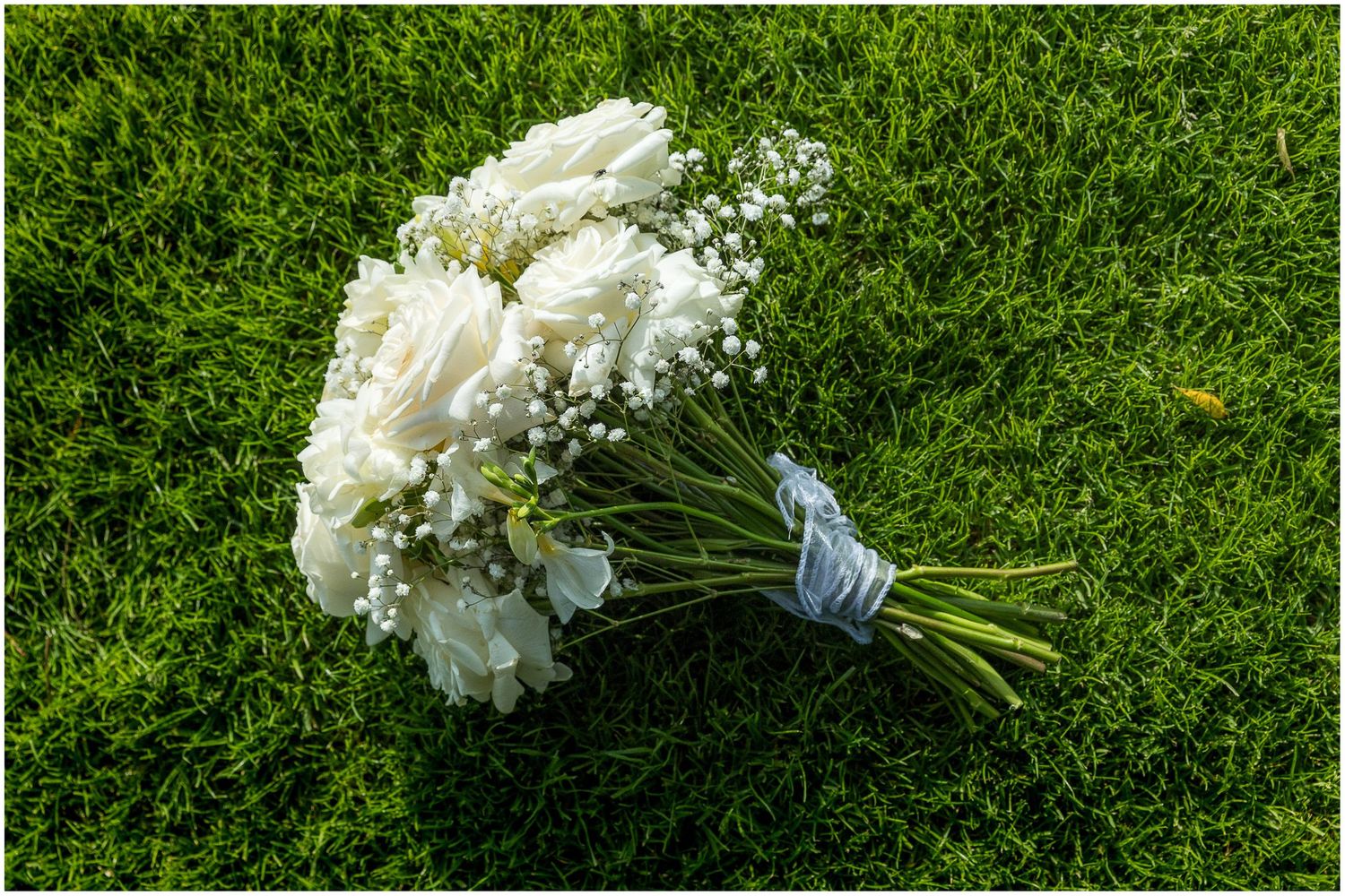 White hydrangea and baby's breath bridal bouquet lying on bright green grass.