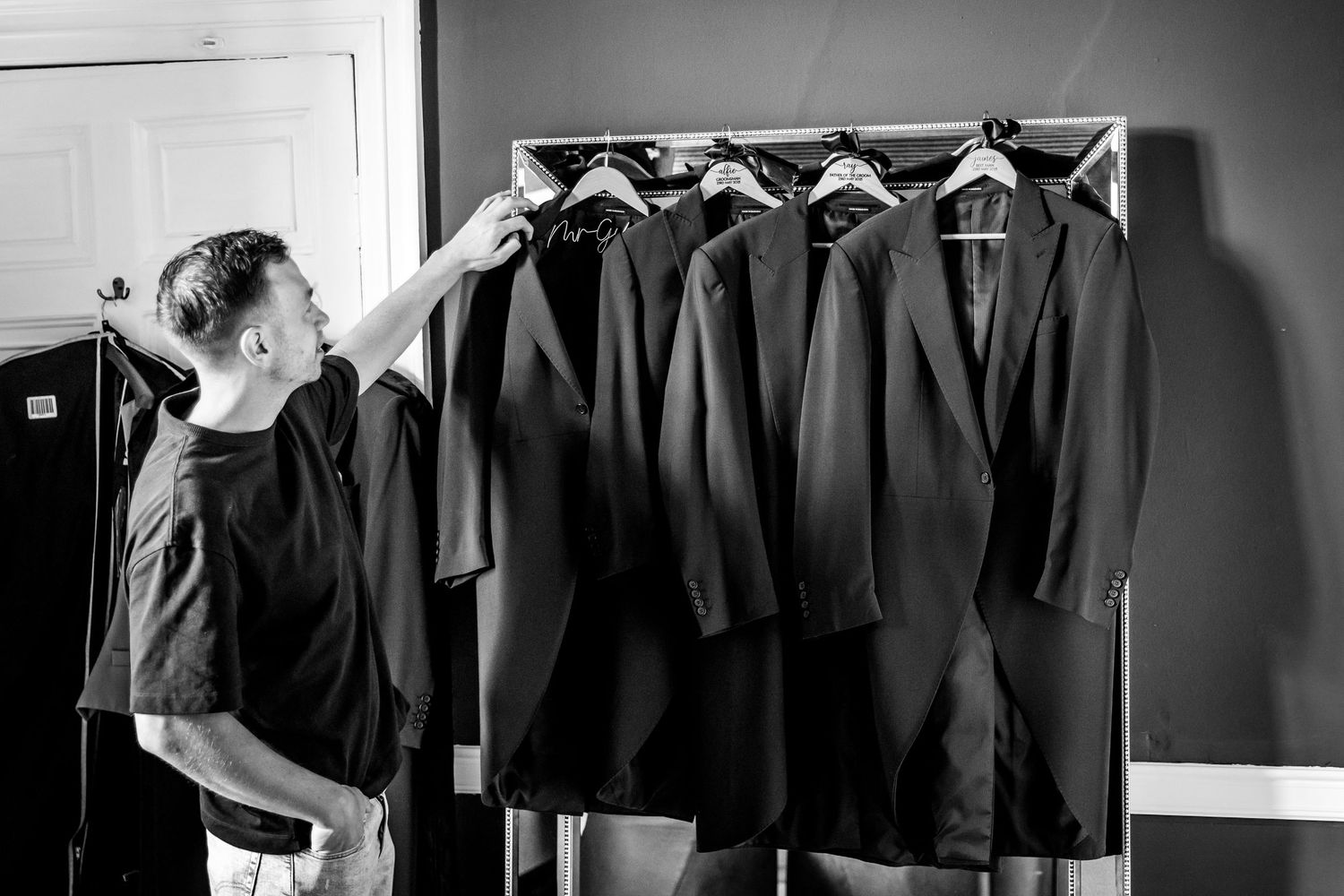 Black and white image of someone organizing dark suits on hangers.