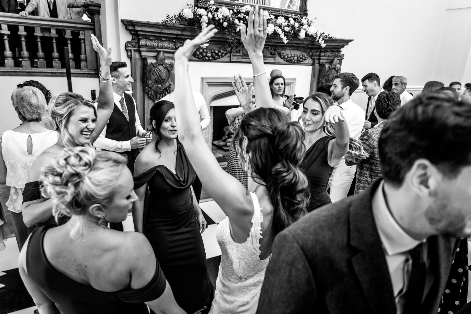 Black and white photo of wedding guests dancing and celebrating on a crowded dance floor.