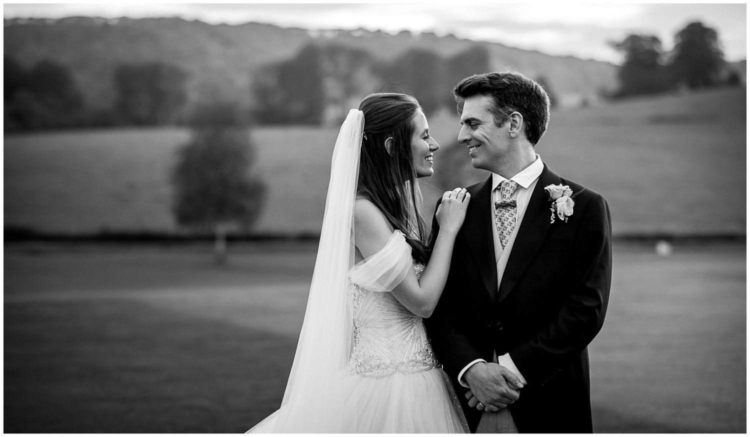 A black and white wedding portrait captures an intimate moment between newlyweds in a pastoral setting.