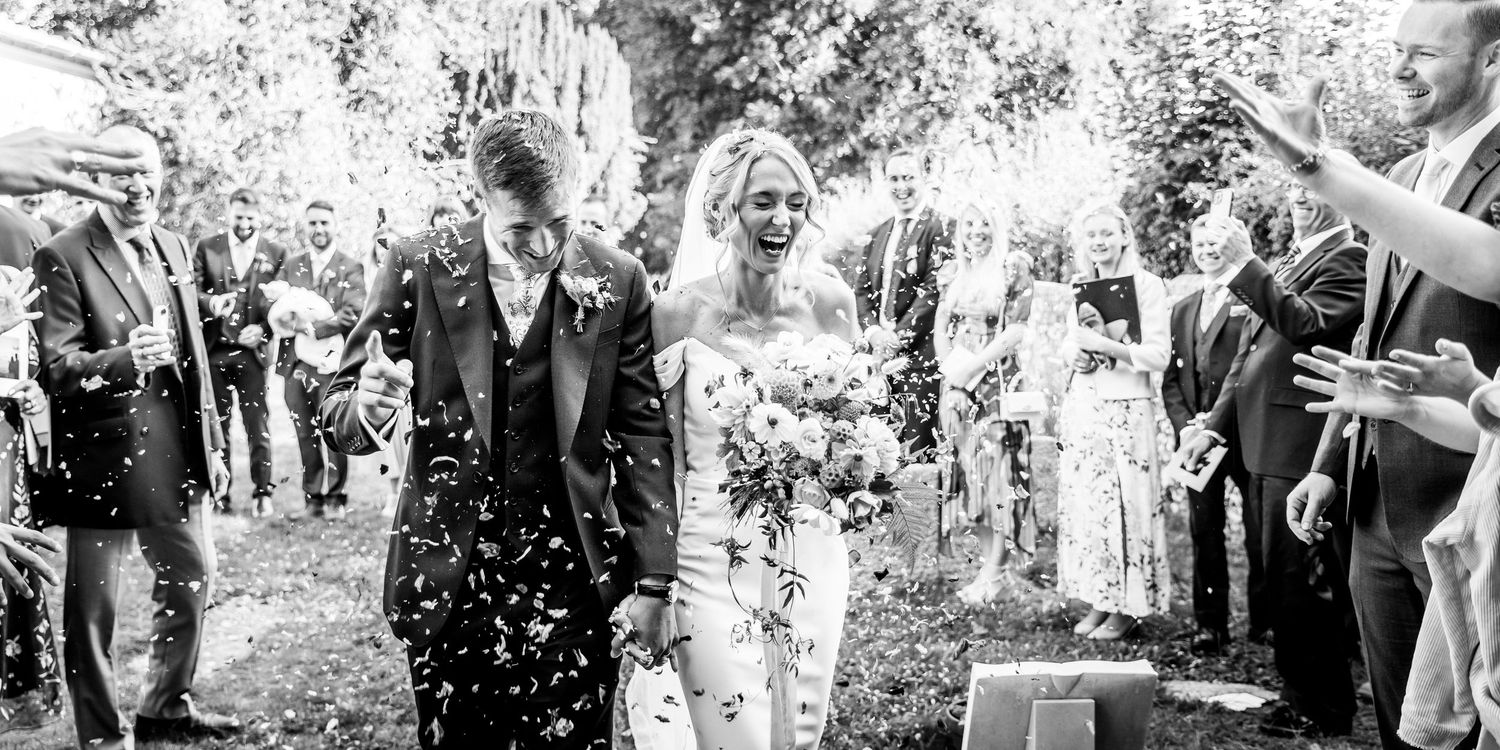 Black and white photo of wedding guests celebrating with confetti outdoors.