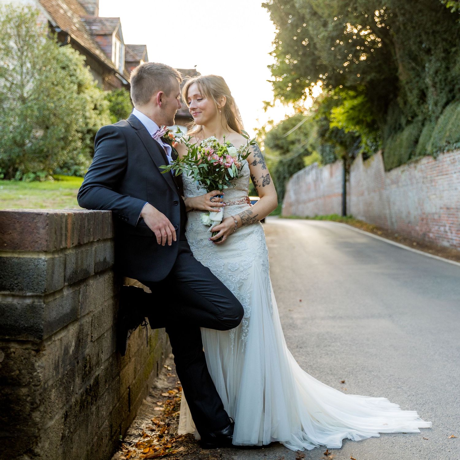 Romantic wedding couple poses for outdoor portraits along a stone wall path at sunset.