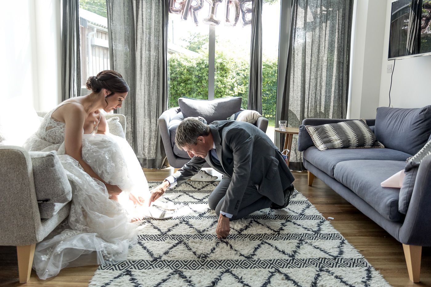 Wedding couple lounging on a modern gray sofa in an indoor setting.