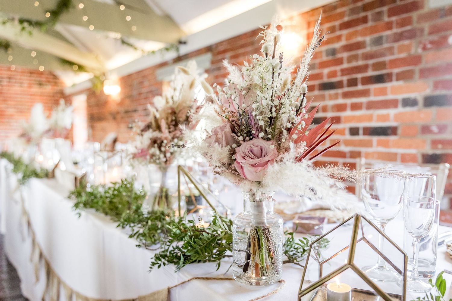 Wedding reception table centerpiece featuring pink and white flowers with geometric gold decor elements.
