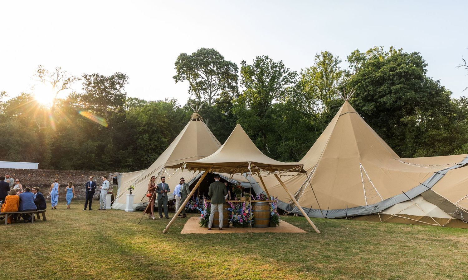 Rustic tipi tents set up in a grassy field during golden hour sunset.