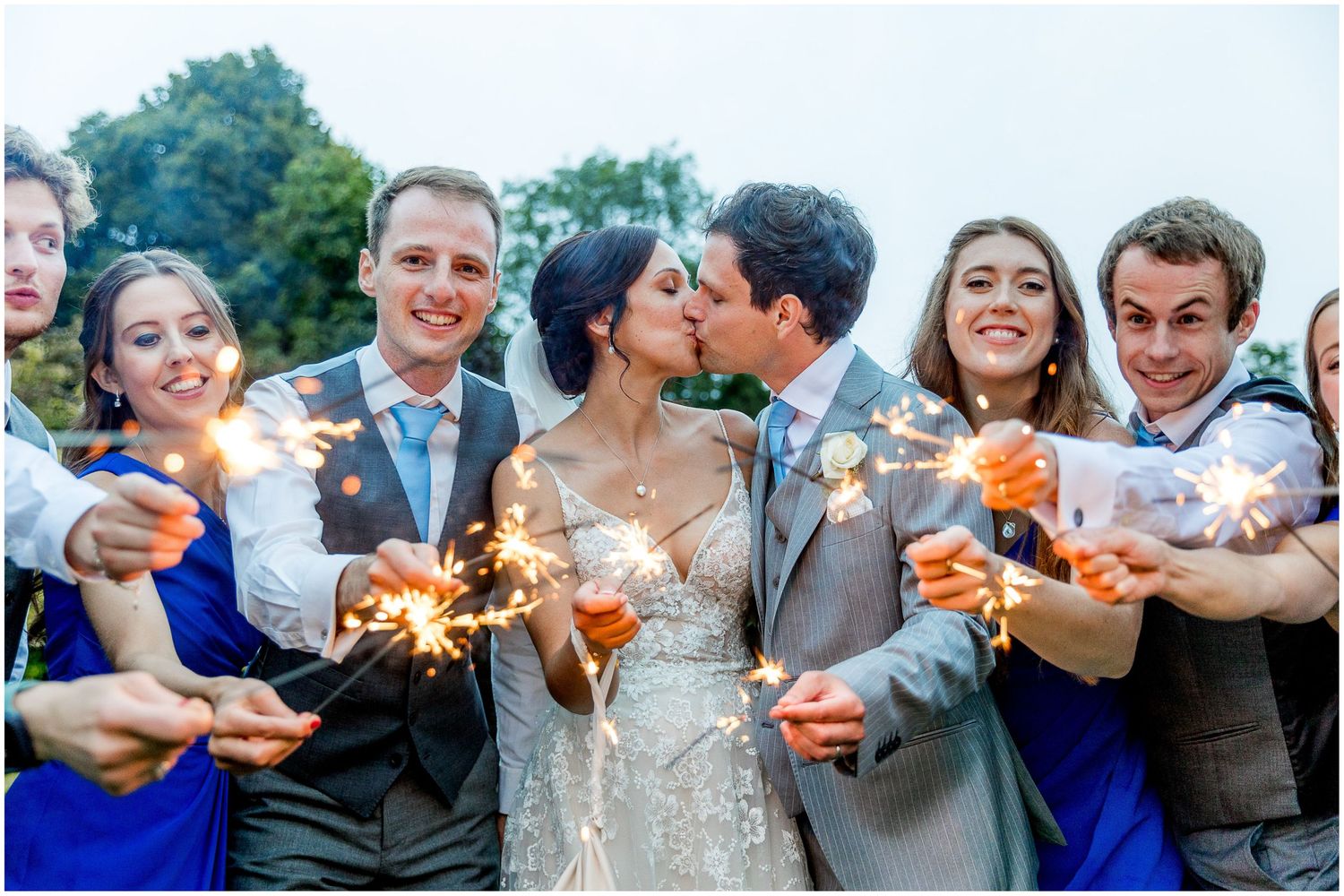 Wedding party members hold sparklers during evening celebration outdoors.