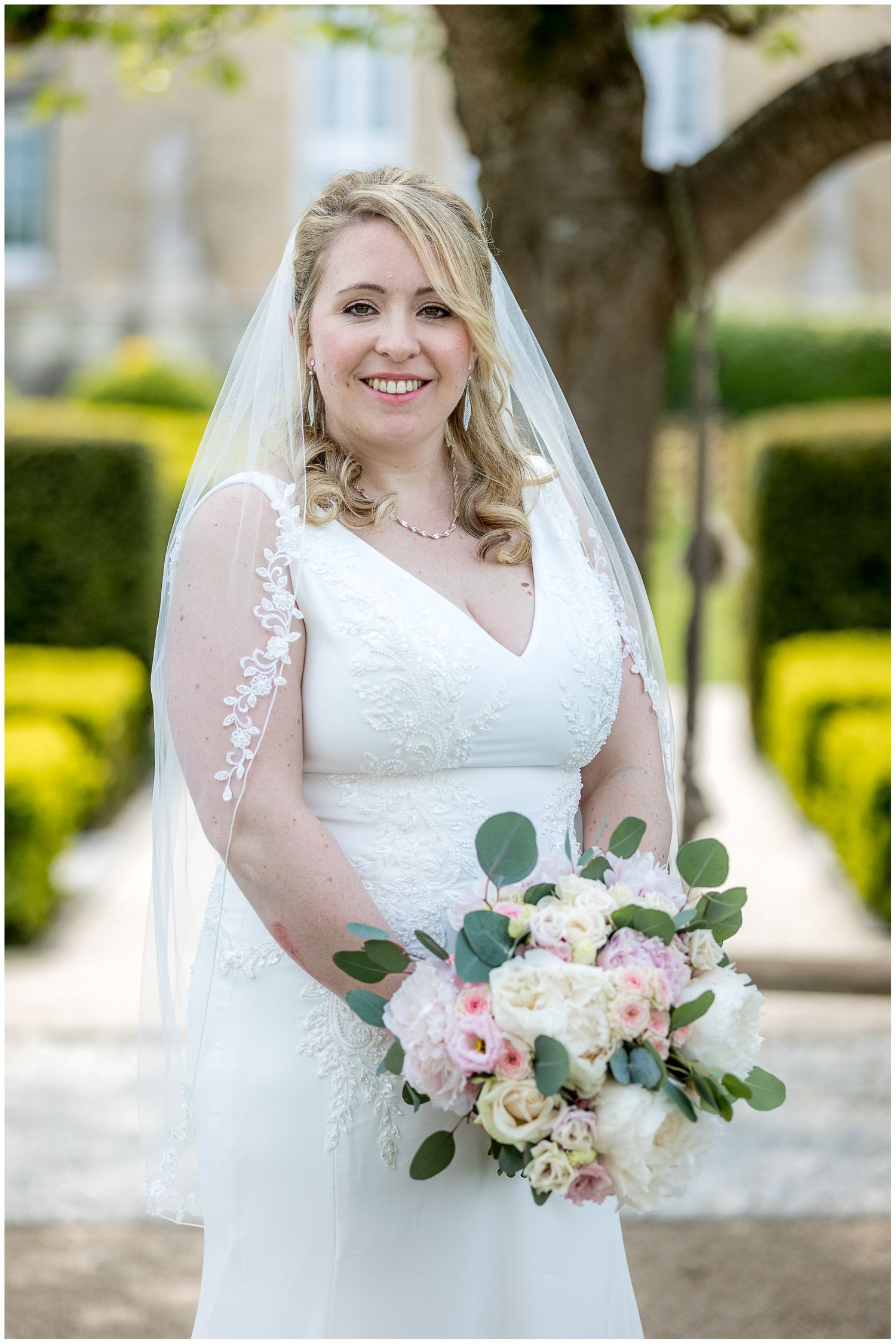 Bride holding delicate pink and white bouquet with eucalyptus in garden setting.