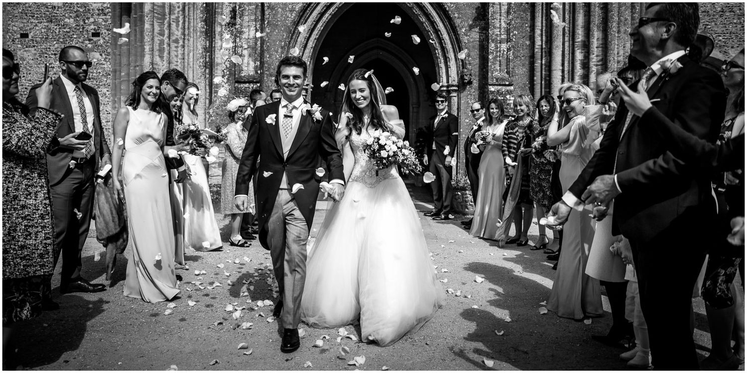 Wedding guests shower the happy couple with flower petals as they exit the church after their ceremony.