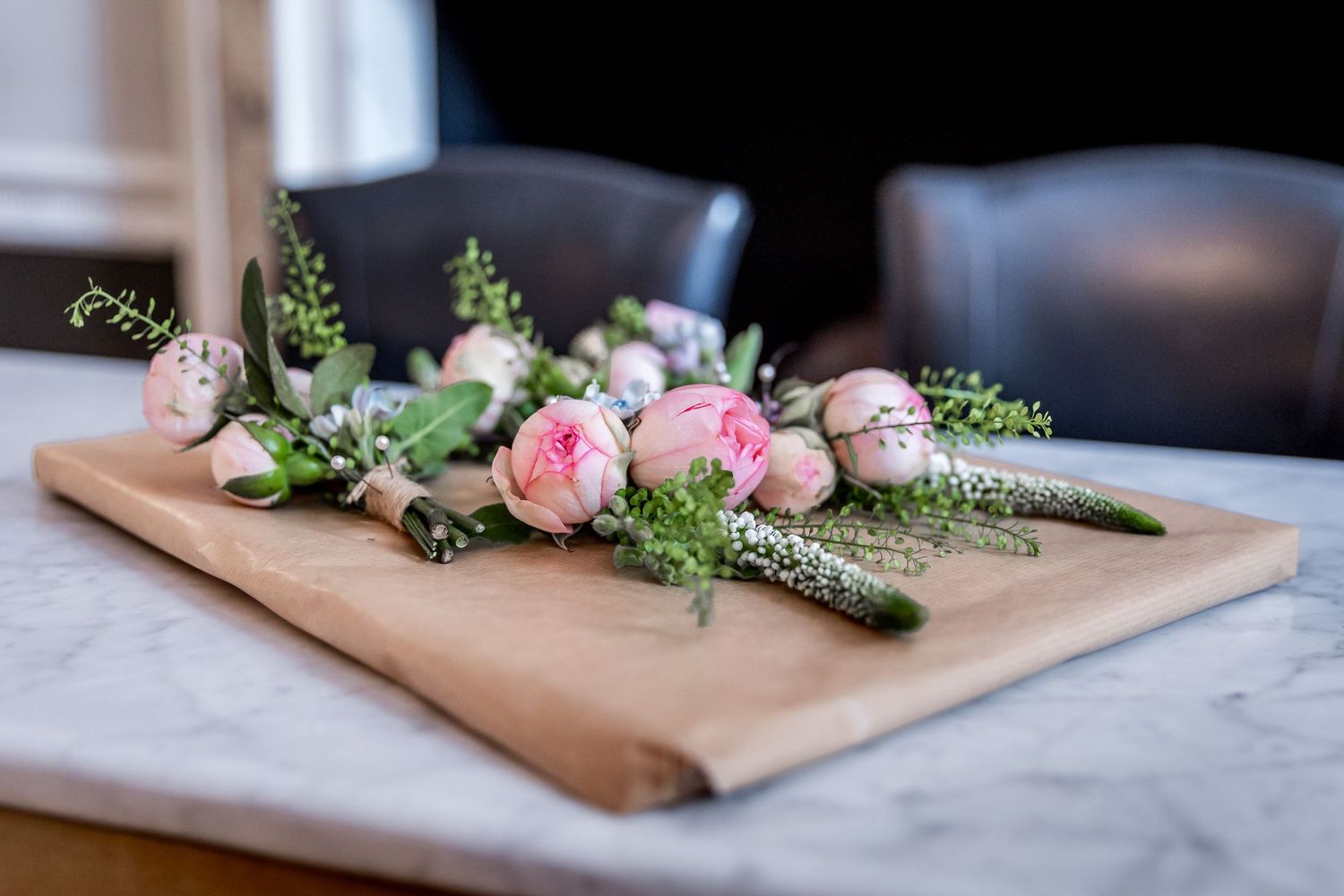 Delicate pink roses and greenery arranged on brown kraft paper.