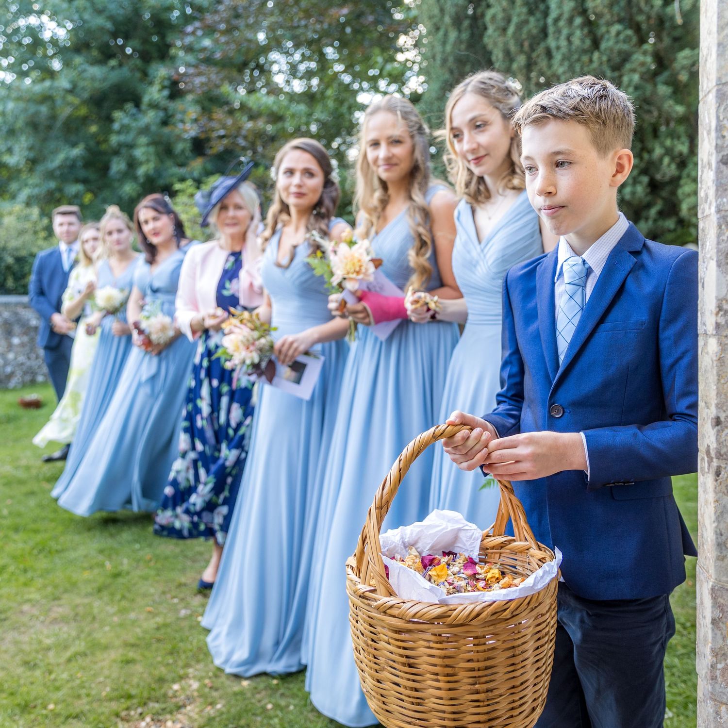 Children in formal attire carrying wicker baskets at outdoor wedding.