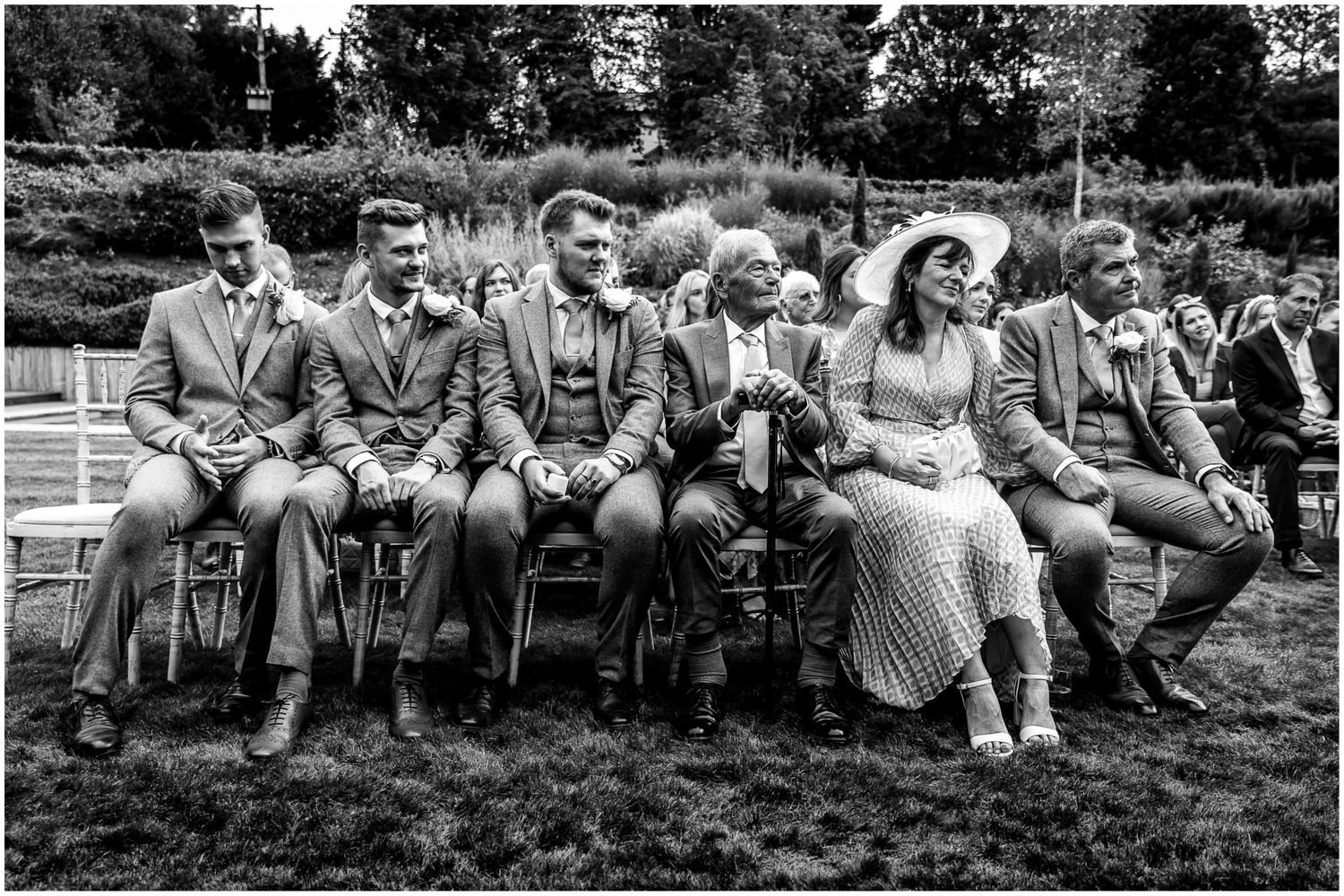 Wide shot of wedding guests sitting on lawn chairs during an outdoor celebration.