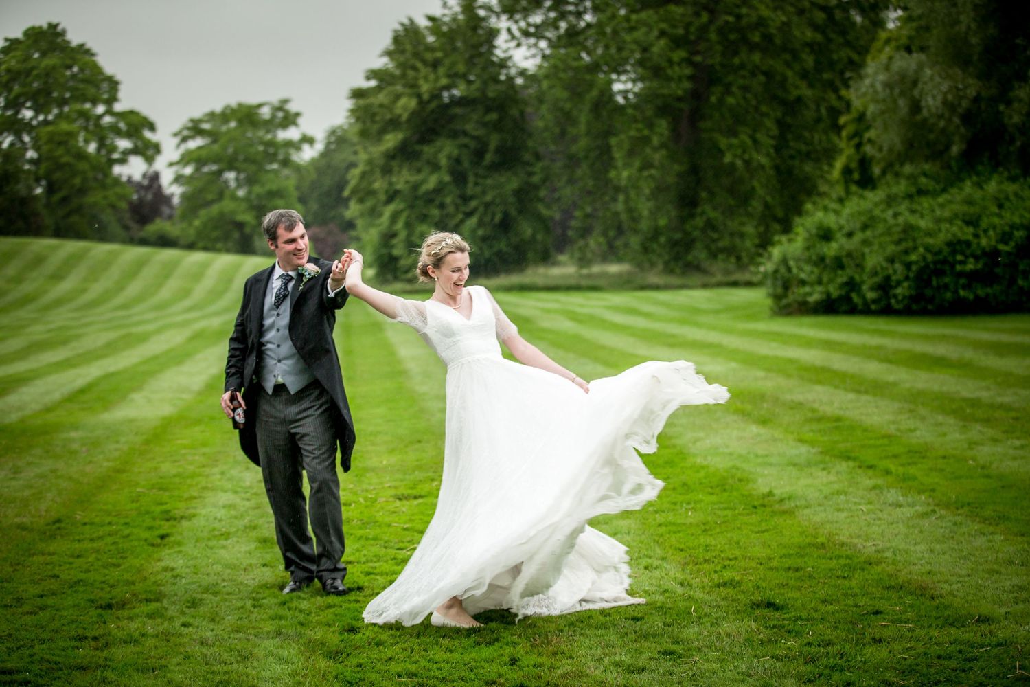 Wedding couple twirls on manicured lawn during outdoor photo session.