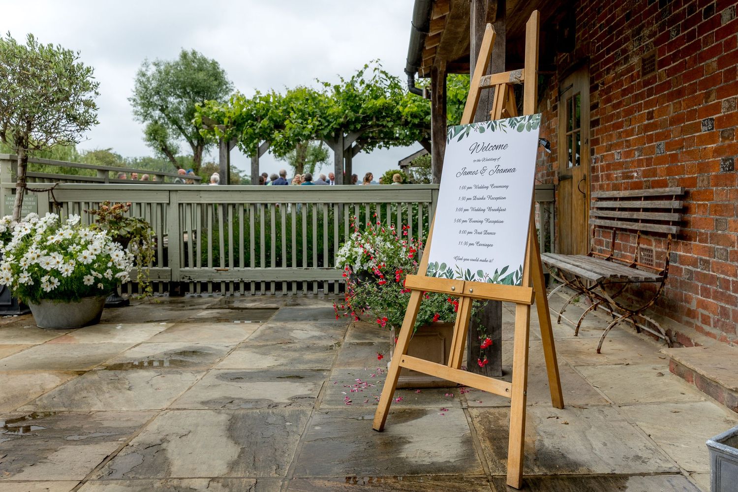 Rustic brick wall venue entrance with wooden signage and garden views.