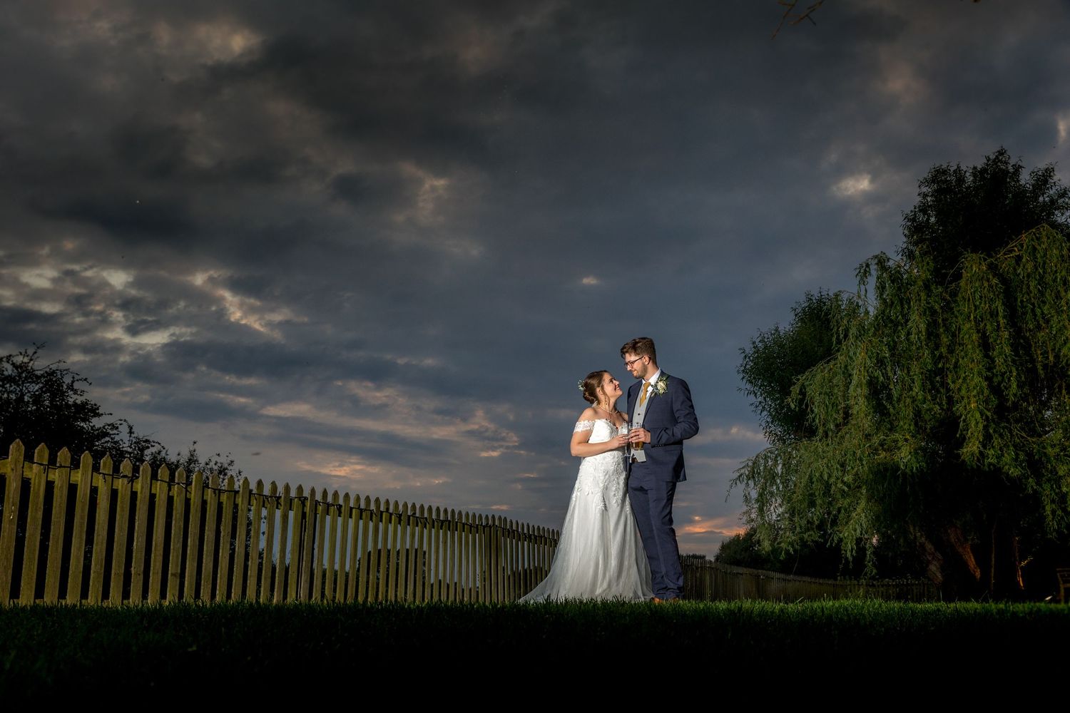 Panoramic view of dramatic storm clouds at sunset with dark silhouettes of trees and fence.
