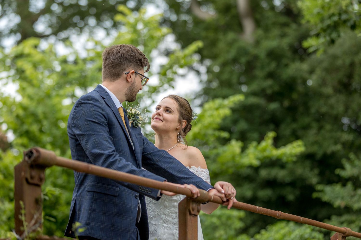 Romantic moment shared on wooden bridge surrounded by summer foliage.