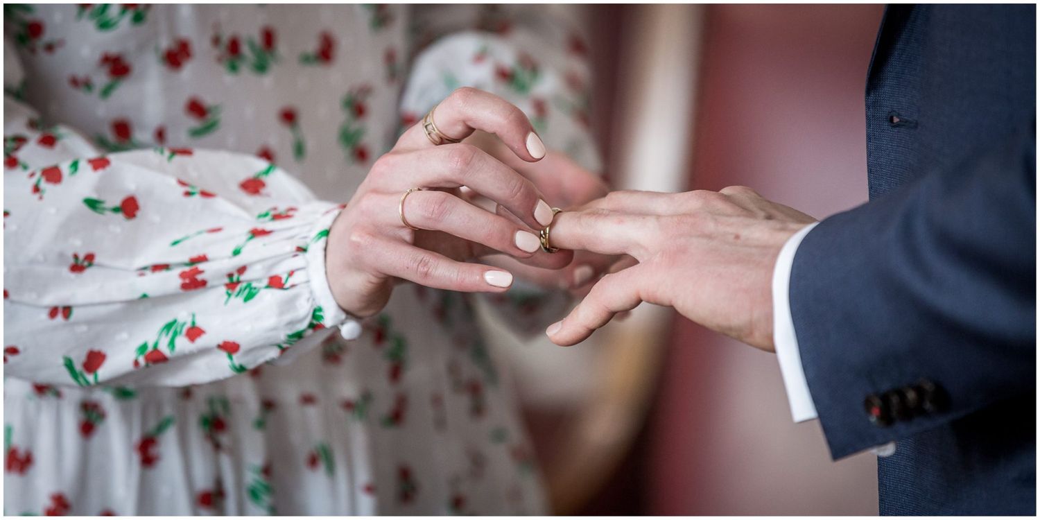 Detail shot of hands during a ring exchange ceremony with floral pattern visible.