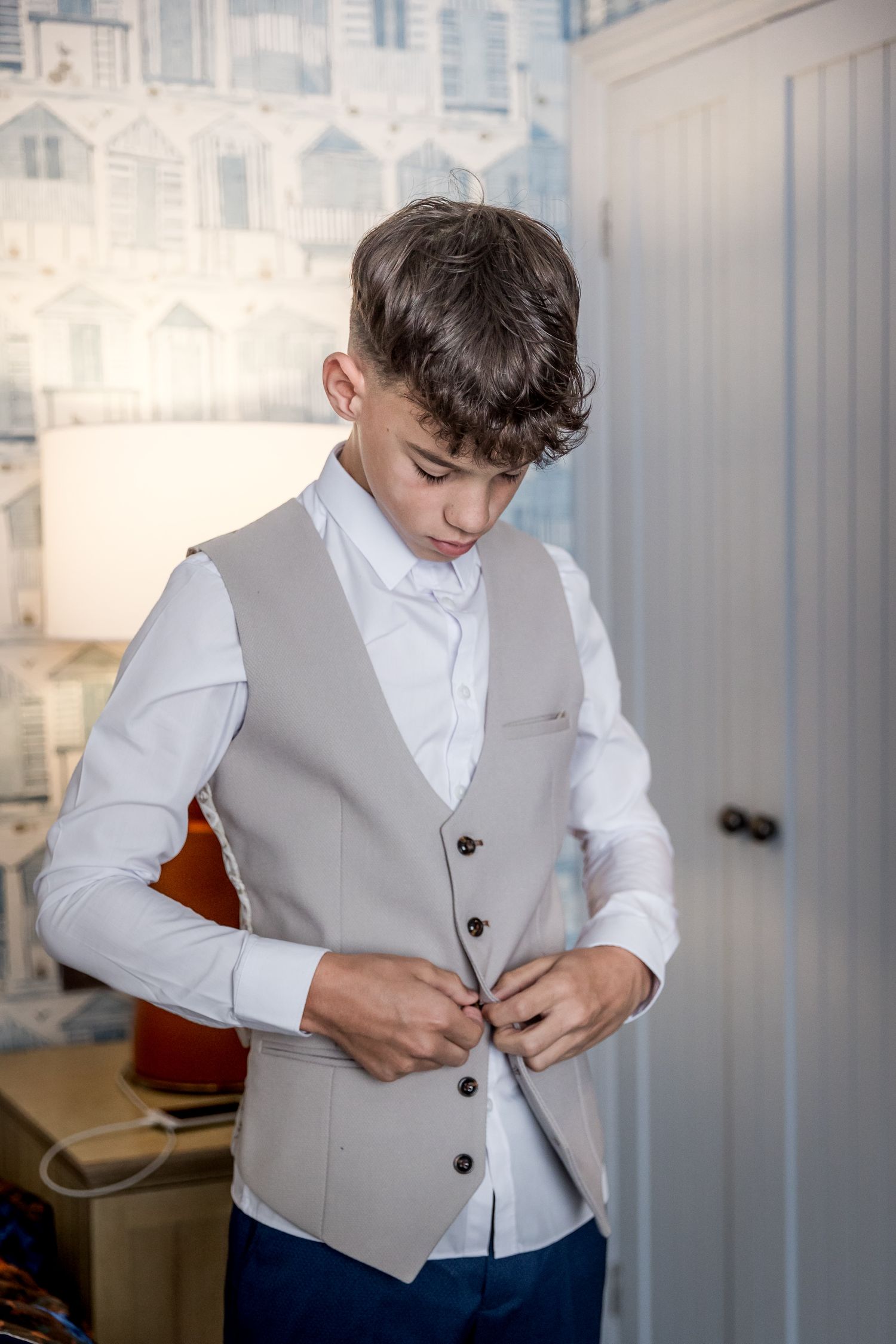 Young person adjusting formal grey vest while getting dressed.