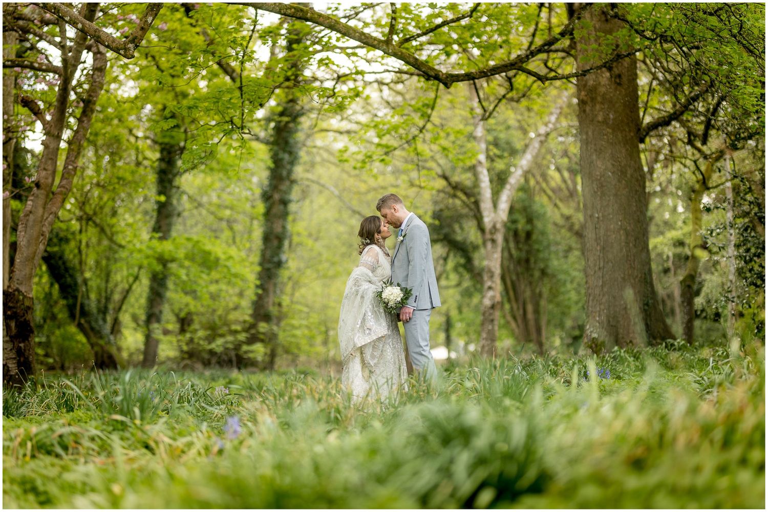 Couple walks hand in hand through a lush green wooded area.