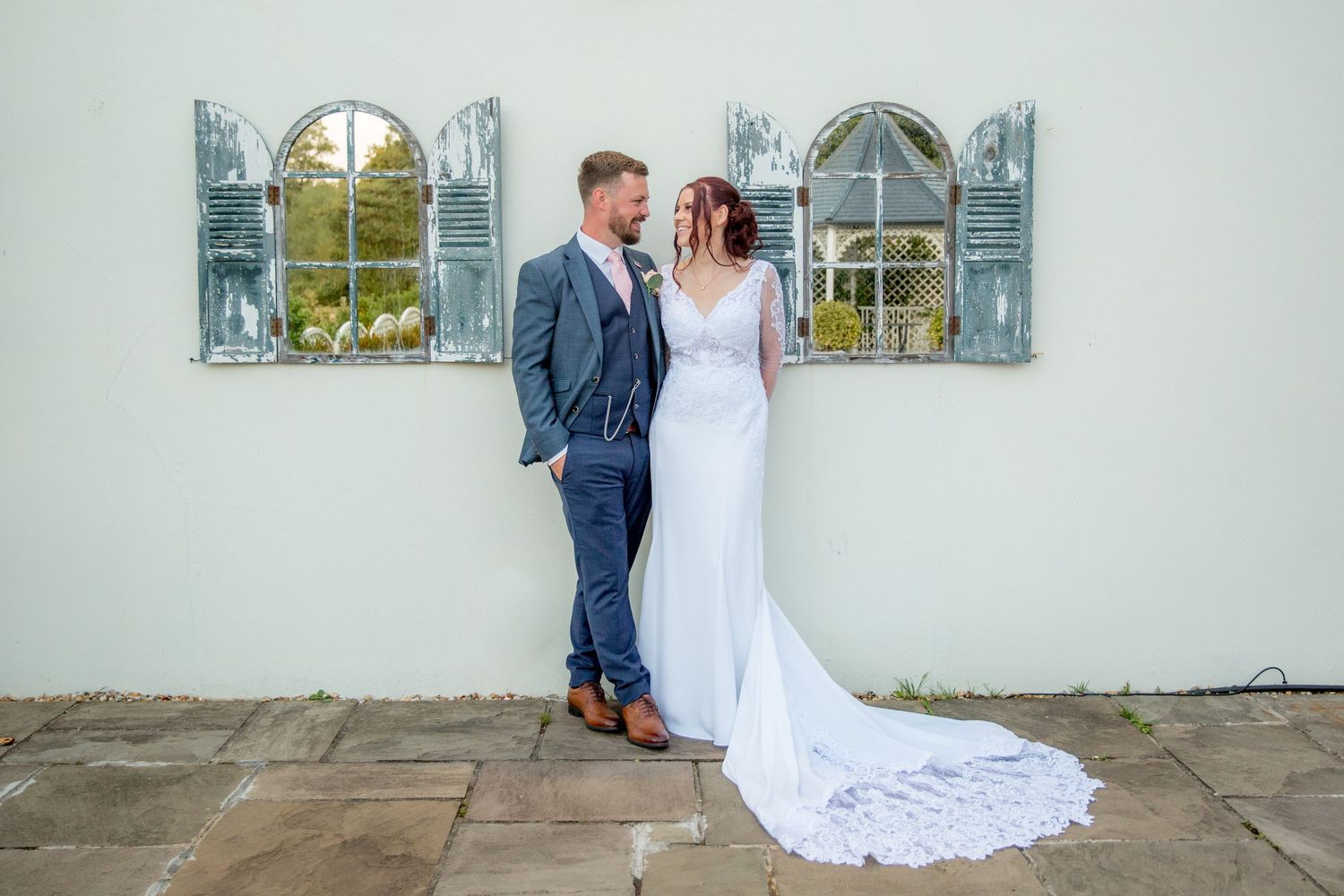 Wedding photos taken against a white church wall with arched windows.