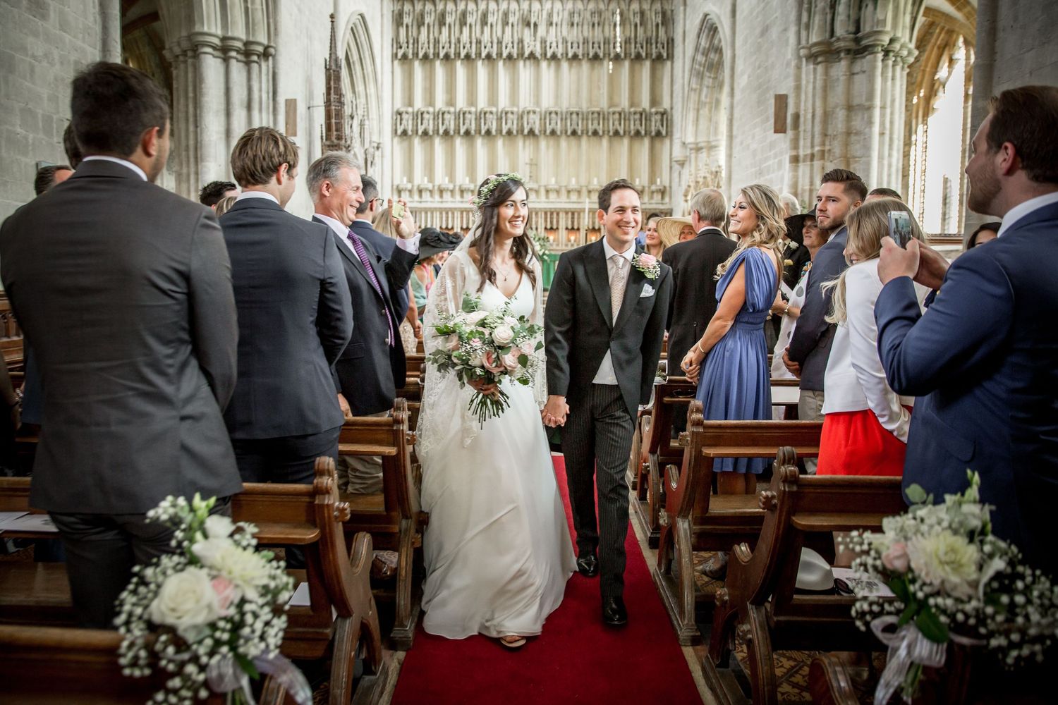 Church wedding ceremony with floral decorations and guests seated in wooden pews.