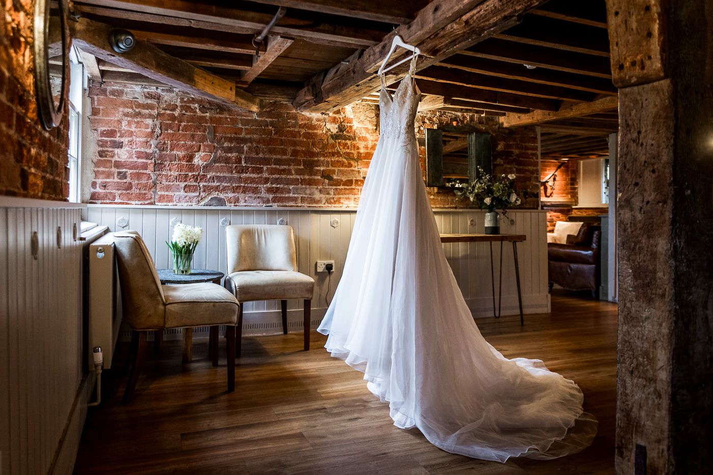 Wedding dress displayed in rustic brick venue with exposed wooden beams and dramatic lighting.